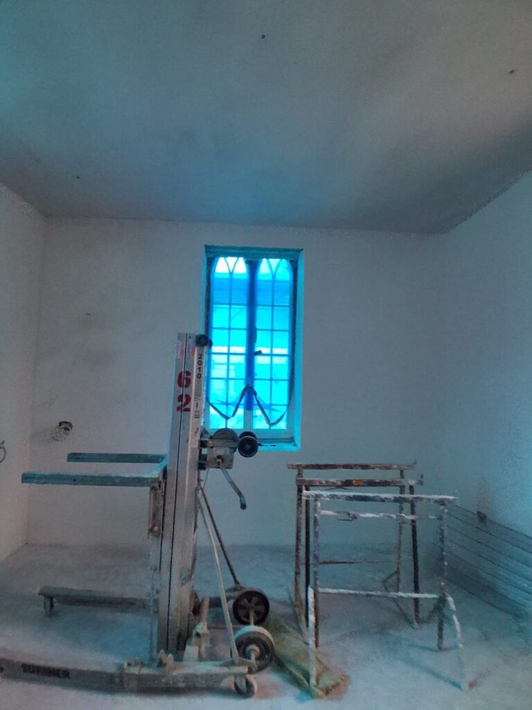 Plastered room with tall window and plasterboard lifter on site