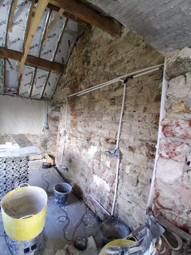 Exposed stone wall with electrical conduits before plastering